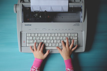 child's hands on a typewriter 