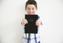 a boy child holding out a Bible 