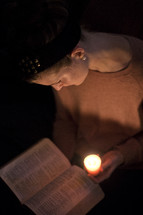 woman reading a Bible by candle light