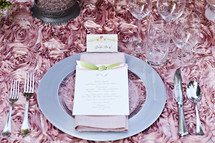 place setting with an invitation, pink table linen, flatware, wedding reception decor place card