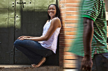 Woman leaning on a brick wall watching a man walk by.