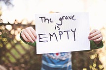 A child holding up a hand written note that says, "The grave is empty."