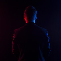 Man in suit facing away with red and blue lights.