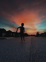 silhouette of a child running down a neighborhood street at dusk 