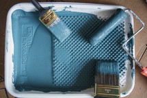 A paint tray filled with blue paint and paint brushes.