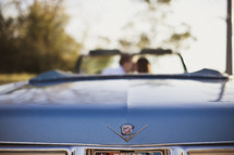 A couple kisses while sitting in a blue cadillac convertible