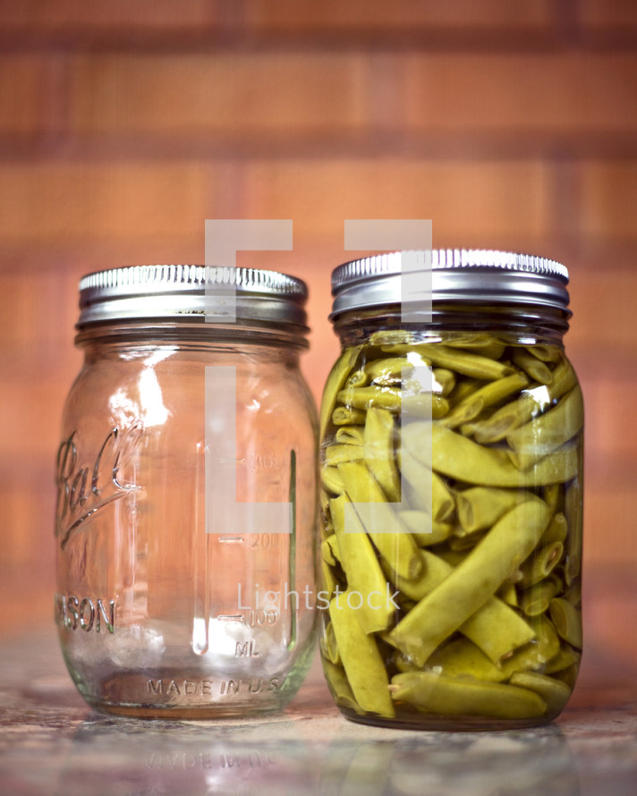 Green beans in a jar by an empty jar.
