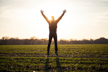man jumping in a field with his hands raised