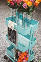 A blue metal cart with bouquets of flowers and a sign reading, "You are a Blessing."