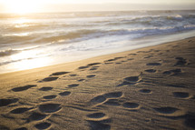 footprints in the sand on a beach at sunrise 