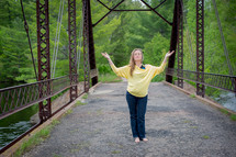woman standing on a bridge with her hands raised to God in worship