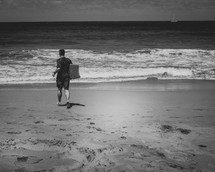 man walking on a beach holding a boogie board 