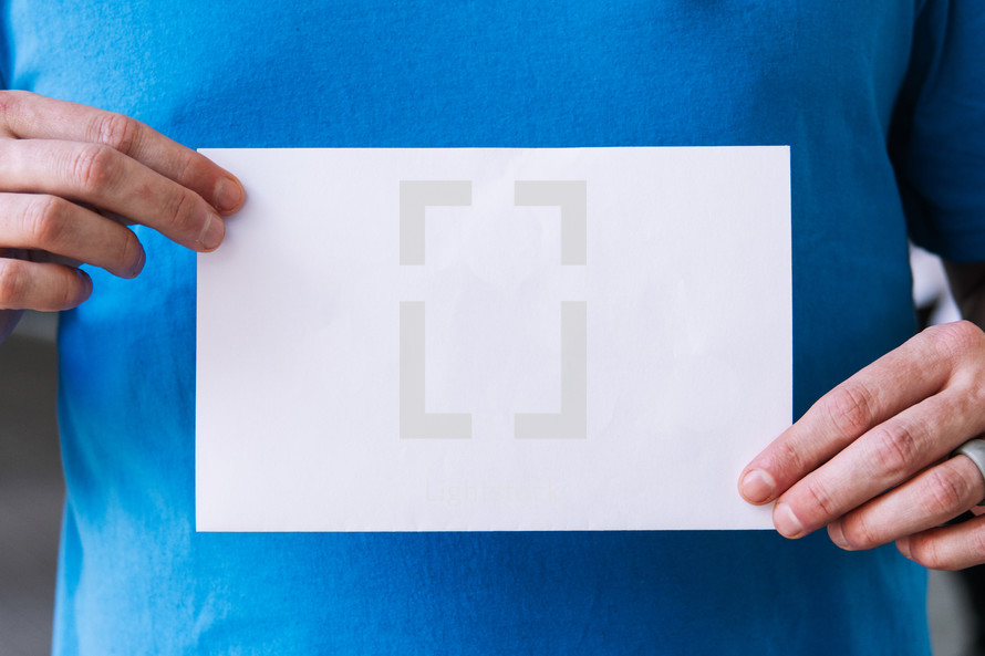 Close up of a man holding up a blank flyer against his torso.