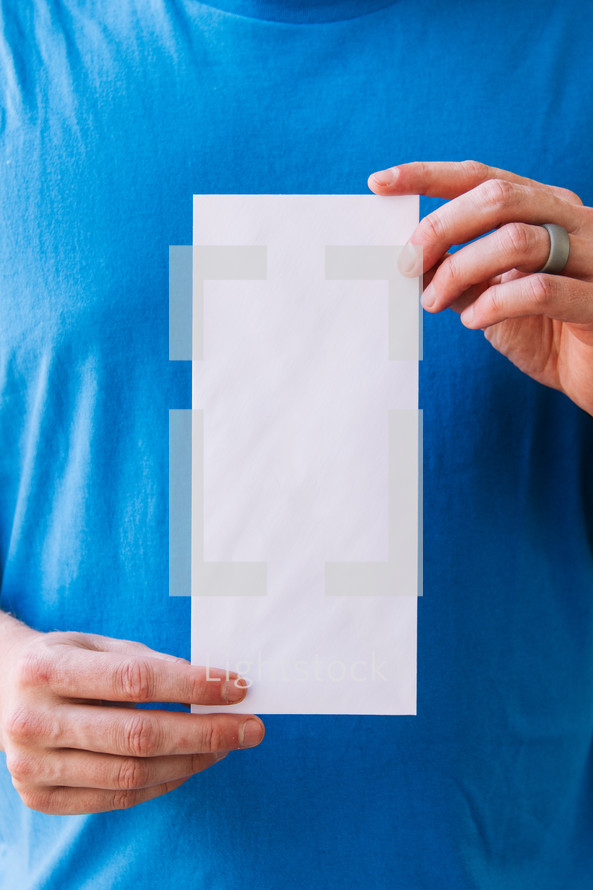 Close up of a man holding up a blank flyer against his torso.