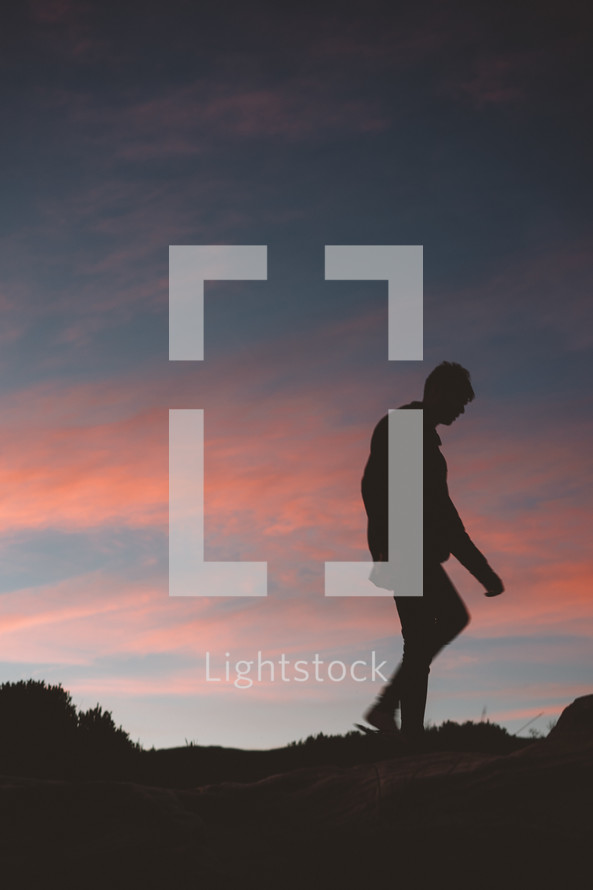 silhouette of a person walking up a hill at sunset 