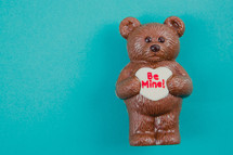 A chocolate bear holding a heart reading "Be Mine!"