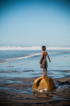 boy child standing on a rock at the beach 