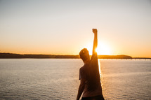 a person standing with a raised fist at the edge of a cliff at sunset 