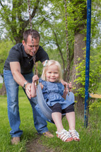 a father pushing his daughter on a swing 