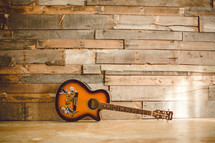 Acoustical guitar on the floor, leaning against the wall.