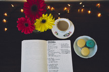 notes in a notebook, gerber daisies, tea, and macaroons
