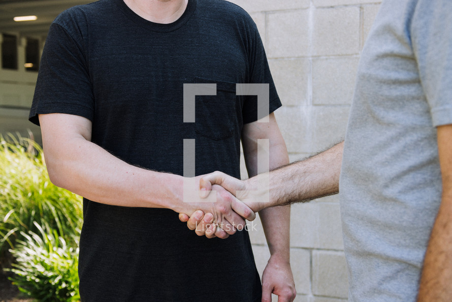 Torso view of two men shaking hands. One is wearing a black pocket tshirt and the other a gray tshirt.