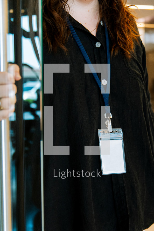 Woman in a black shirt wearing a lanyard while holding a door open.