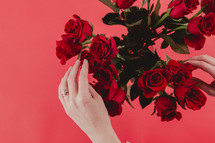 A woman's hands touching a bouquet of red roses.