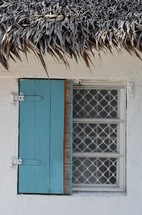 blue shuttered window  of house with thatch roof