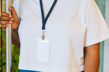 Woman in a white tshirt wearing a large lanyard while holding a door open.