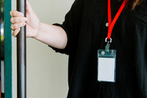 Woman in a black shirt wearing a lanyard while holding a door open.