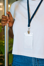 Woman in a white tshirt wearing a large lanyard while holding a door open.