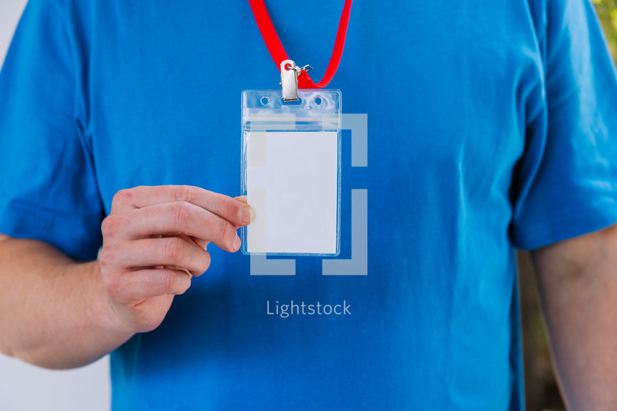 Man in a blank blue tshirt holding up a lanyard.