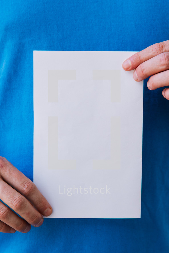 Close up of a man holding up a blank flyer against his torso.