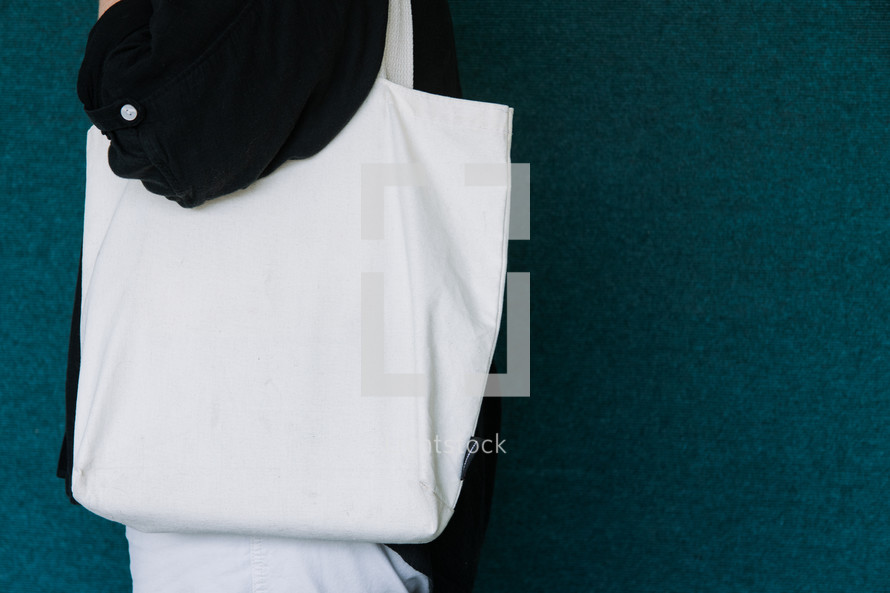 Woman in a black shirt holding a blank canvas tote bag on her shoulder.