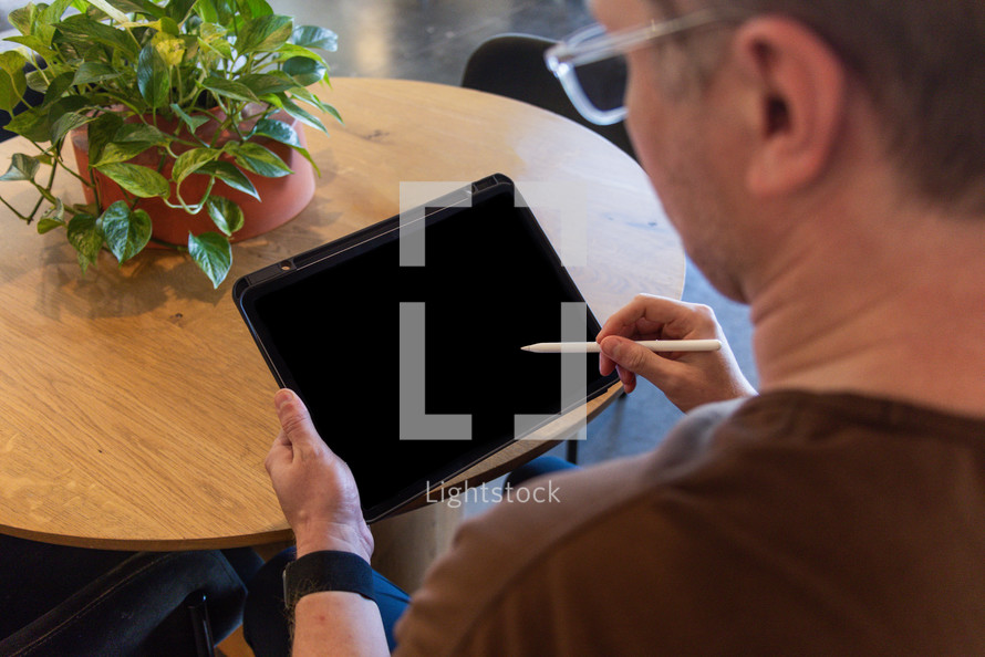 Over the shoulder view of a man holding an iPad pencil against an iPad screen.