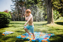 child playing in a sprinkler 