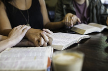 girls holding hands in prayer around a table at a Bible study 