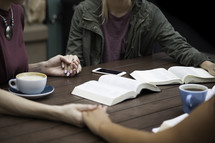 girls holding hands in prayer around a table at a Bible study 