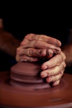 Hands molding clay on a potter's wheel