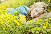 A young woman lying in a field of yellow flowers.
