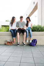 college students on campus sitting reading a book 