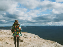 a woman standing on a mountaintop under a cloudy sky 