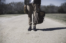 man standing on a gravel road holding a map and backpack 