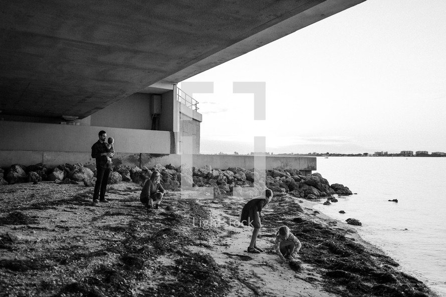 a family walking along a shore under an overpass 