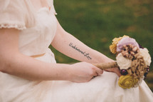 A bride with a tattoo holding a bouquet of flowers
