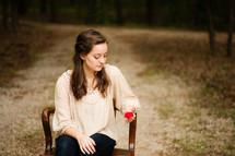 young woman sitting in a chair holding a red rose 