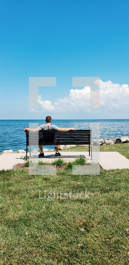 a man sitting on a bench over looking the water 