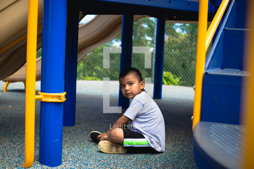 child sitting under a slide on a playground 