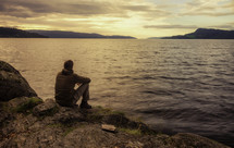 a man sitting on a rocky shore praying 